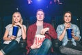 Three beautiful people are sitting in chairs and watching movie. They look happy and excited. Girls are drinking cola Royalty Free Stock Photo