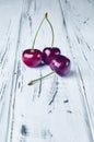 Three beautiful red cherries on a white wooden table Royalty Free Stock Photo