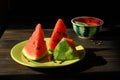 Three beautiful triangular slices of watermelon with juicy red pulp and black seeds on a green dish on a wooden table.