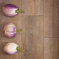 Three beautiful white and purple Bianca eggplants lying on a wood texture tile