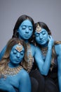 Three South Asian women painted blue and wearing gold jewellery