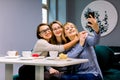 Three beautiful young women enjoying coffee and cake together in a cafe sitting at a table laughing and making selfie Royalty Free Stock Photo