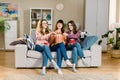 Three beautiful young women friends at home eating popcorn sitting on gray sofa together and laughing. Home women party Royalty Free Stock Photo