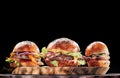 Three beef burgers with tomatoes, cheese, red onions on wooden cut on black background. Burgers menu. Space for text. Royalty Free Stock Photo