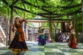 Three belly dancers with swords perform on wooden platform under vined trellis for onlookers in