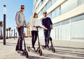 Three best friends young 20s -30s girl and guys spend time outdoors gathered together driving on electric scooter Royalty Free Stock Photo