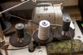 Three big black and white bobbins with large mating threads mounted on a rod near the sewing machine on the table of the workshop