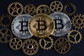 Three bitcoins among various cog wheels. Cryptocurrency concept..
