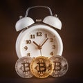 Three bitcoins and vintage white alarm clock glowing on black background.