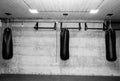 Three black punching bags in the empty boxing gym with naked grunge wall in background black and white