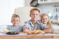 Three blonde kids twoboys and girl on kitchen at home. Family eating healthy food , green salad on plates. Looking at Royalty Free Stock Photo