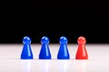 Three plastic blue game pieces and a red figure standing next to them as a leader, boss or different. Blurred black and white Royalty Free Stock Photo