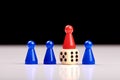 Three blue game pieces and between them one red piece stands on a dice as a winner or leader. Black and white background