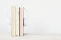 Three books and hearphones on a wooden shelf against a white background. Reading concept and study metaphor with empty copy space