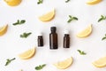 Three bottles of essential oil surrounded with fresh herbs green mint leaves and lemon lobules. flat lay on a white