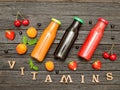 Three bottles with juice, fruit and inscription vitamins on a wooden background, food concept Royalty Free Stock Photo