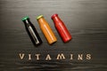 Three bottles with juice and inscription vitamins on a black wooden background, food concept Royalty Free Stock Photo