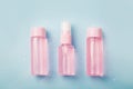 Three bottles of pink tonic or lotion sprinkled with water on blue background