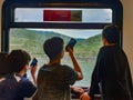 Three boys are looking out of their train window taking photos on their mobile phones as the train rides along the Rhine Valley