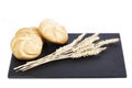 Three bread rolls next to some ears of wheat on a blackboard on a white background