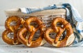 Three brezels or pretzels placed near bread basket with napkin on white wooden background