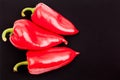 Three bright big red bell peppers with gteen tails on black background top view closeup