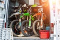 Three bright dirty sport motocross motorcycles stand in tail of technical support assistance van in team camp during extreme Royalty Free Stock Photo