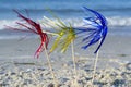 Three bright shiny colored cocktail decorations on stick stand in sand near sea Royalty Free Stock Photo