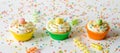 Three brightly colored homemade cupcakes on a white wooden background with sprinkles