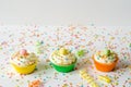 Three brightly colored homemade cupcakes on a white wooden background with sprinkles