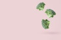 Three broccoli heads fall freely on a pink background casting a light shadow.