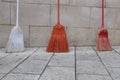 Three brooms of different colors against a wall