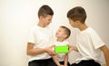 Three brothers with smartphone three boys in white t-shirts sit hold a phone with a green chromakey screen in front of Royalty Free Stock Photo