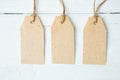 Three brown blank paper price tags or labels set hanging on a rope on the blue wooden background. Royalty Free Stock Photo