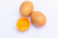 Three brown eggs With one egg broken in half, with a yolk inside the eggshell, laid on a white background Royalty Free Stock Photo