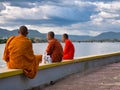 Three Buddhist monks sit next to the Preaek Tuek Chhu River at Kampot, Cambodia
