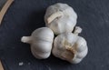 Three bulbs of garlic lie on a stone cutting board. Close-up. View from above