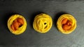 Three bunches of pasta fettuccine on a black background, raw yellow egg pasta nest with red shells concilia from the dough Royalty Free Stock Photo