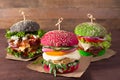 Three burgers with different bread buns red, green, black on wood background Royalty Free Stock Photo