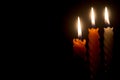 Three burning candle flames or lights glowing on spiral white and orange candles on black or dark background on table in church Royalty Free Stock Photo