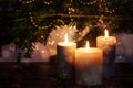 Three burning candles in front of dark fir branches with Christmas decoration and bokeh bubbles, seasonal holiday greeting card,