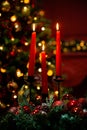 Three burning red candles in the dark against the bokeh of a Christmas tree, lights and decorations Royalty Free Stock Photo