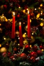 Three burning red candles in the dark against the bokeh of a Christmas tree, lights and decorations Royalty Free Stock Photo