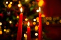 Three burning red candles in the dark against the bokeh of a Christmas tree, lights and decorations Royalty Free Stock Photo