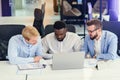 Three businessmen sitting at the modern office tables and analysing data from report and computer to succeed in