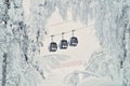 Three cable cars or gondola lifts going up the slope, pictured through the snow-covered trees. Beautiful snowy winter landscape in