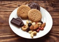 Three cakes, variety of nuts and two chocolate on the white plate on wooden table.