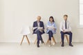 Three candidates of different ages and ethnicities sitting on chairs waiting for job interview