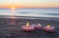 Three candles in shape of heart burn on sand on the sea beach near the sea waves