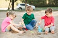 Three Caucasian children sitting in sandbox playing with beach toys. Little girl and boys friends having fun together on Royalty Free Stock Photo